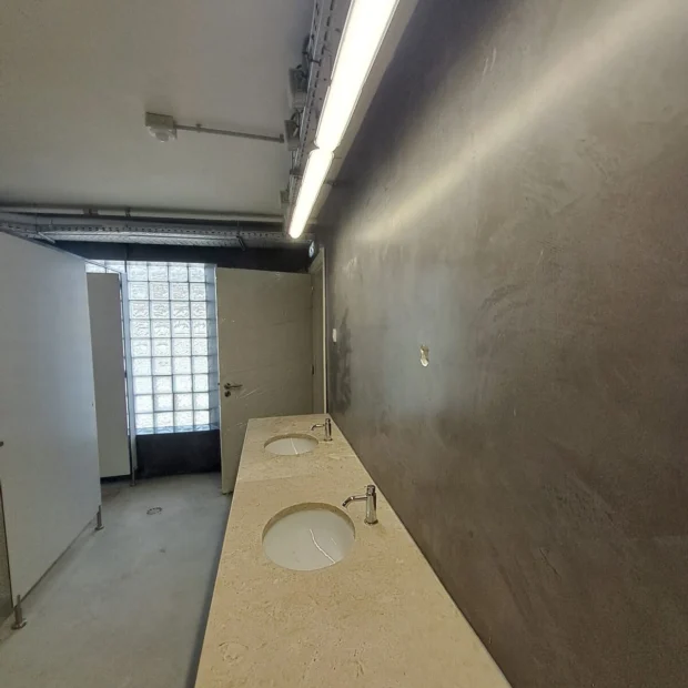 Corredor de sanitários com parede em microcimento escuro
